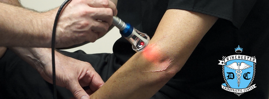 A doctor is administering the red laser therapy upon a patient's left elbow.